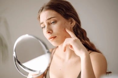 Woman looking at acne scars in the mirror